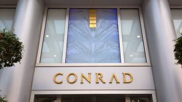Exterior de um edifício com o nome 'CONRAD' em destaque em letras douradas.