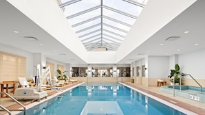 An indoor swimming pool with a skylight ceiling, lounge chairs, and a view of the interior. - Conrad Indianapolis (Indianapolis)