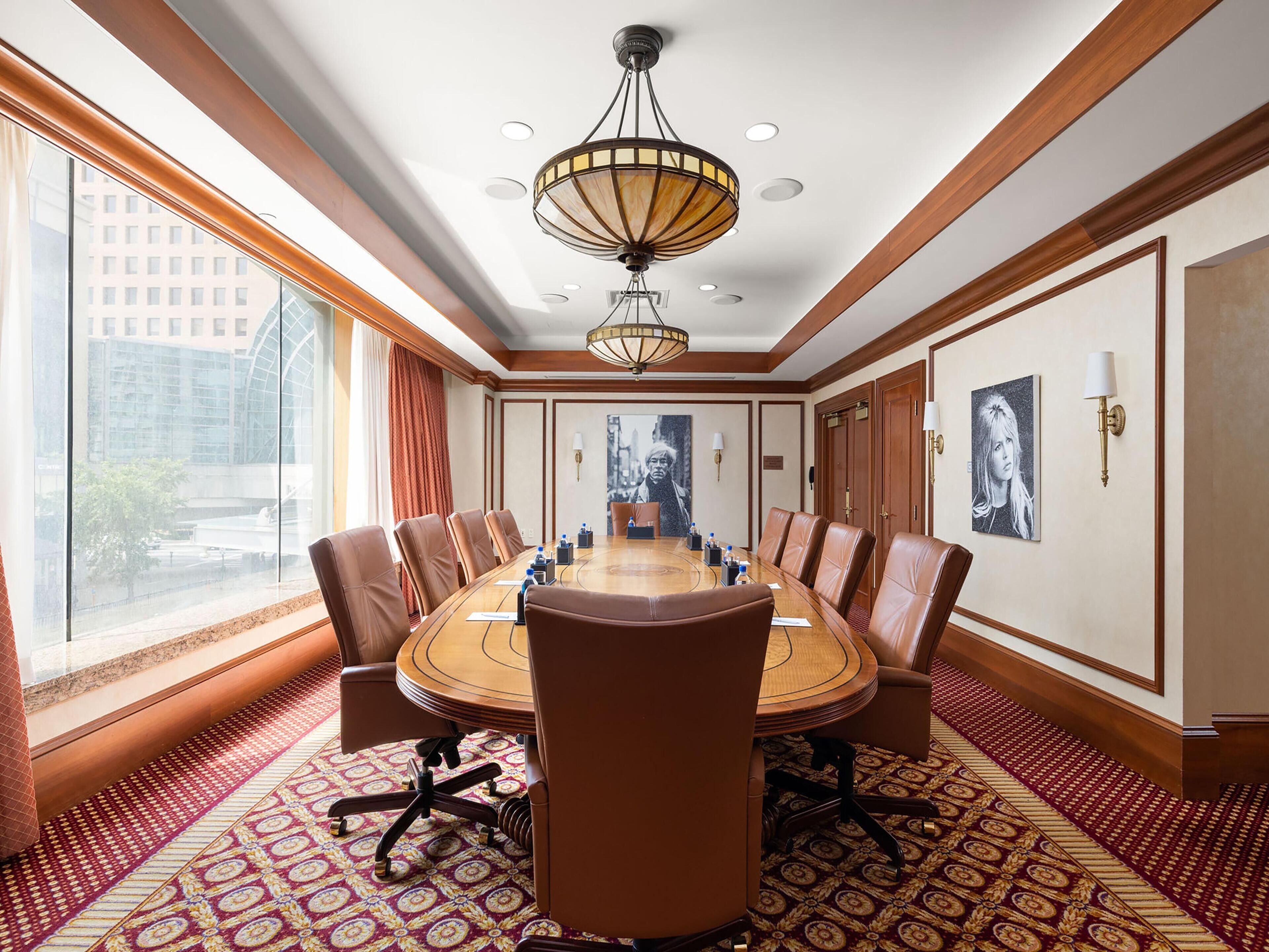 A conference room with a large oval table, leather chairs, a chandelier, and large windows with curtains.