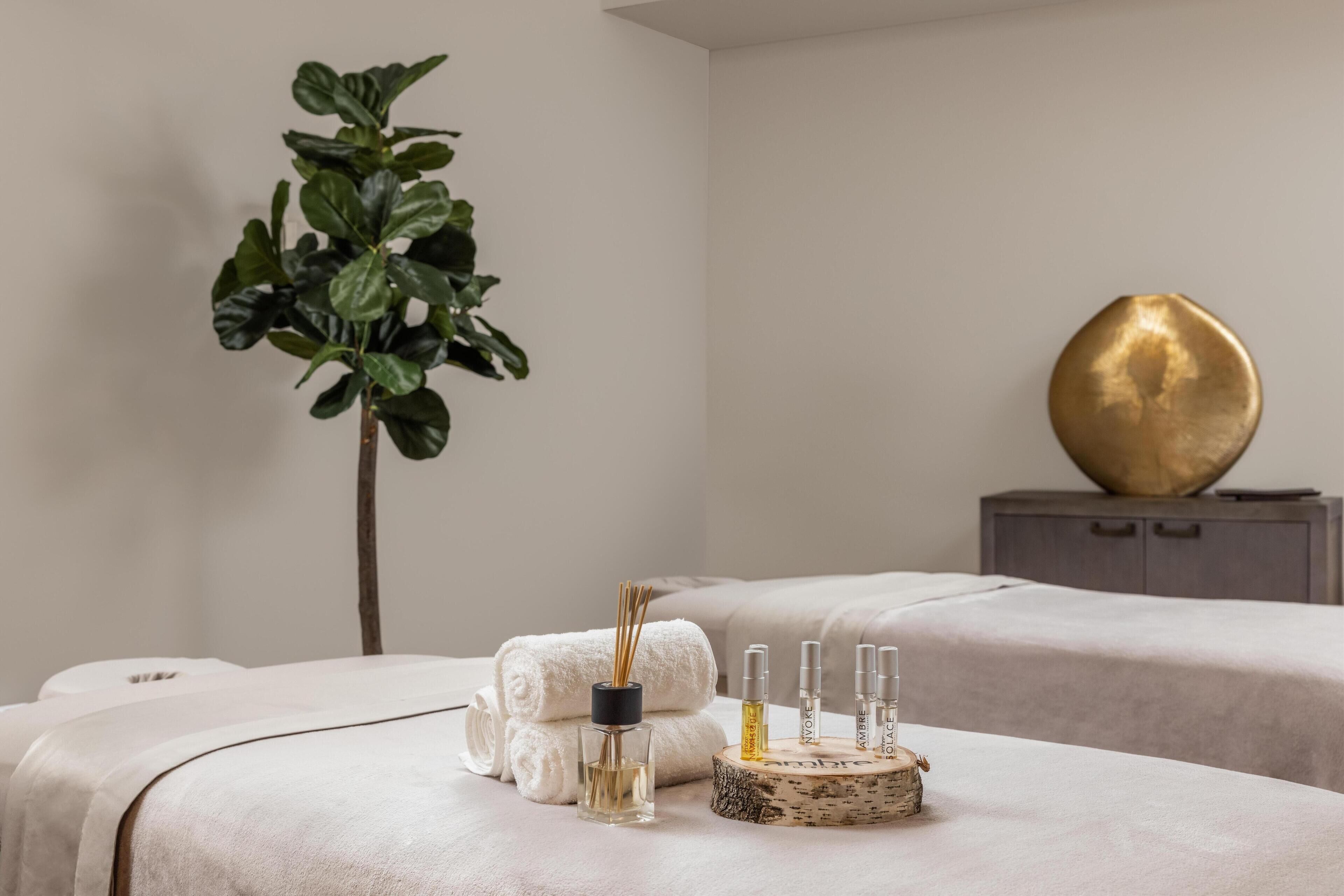 A spa room with two massage tables, a plant, a decorative wooden bowl, and a gold ornament on a cabinet.