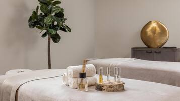 A spa room with two massage tables, a plant, a decorative wooden bowl, and a gold ornament on a cabinet.