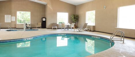 An indoor swimming pool with clear water, surrounded by lounge chairs and a table with chairs.