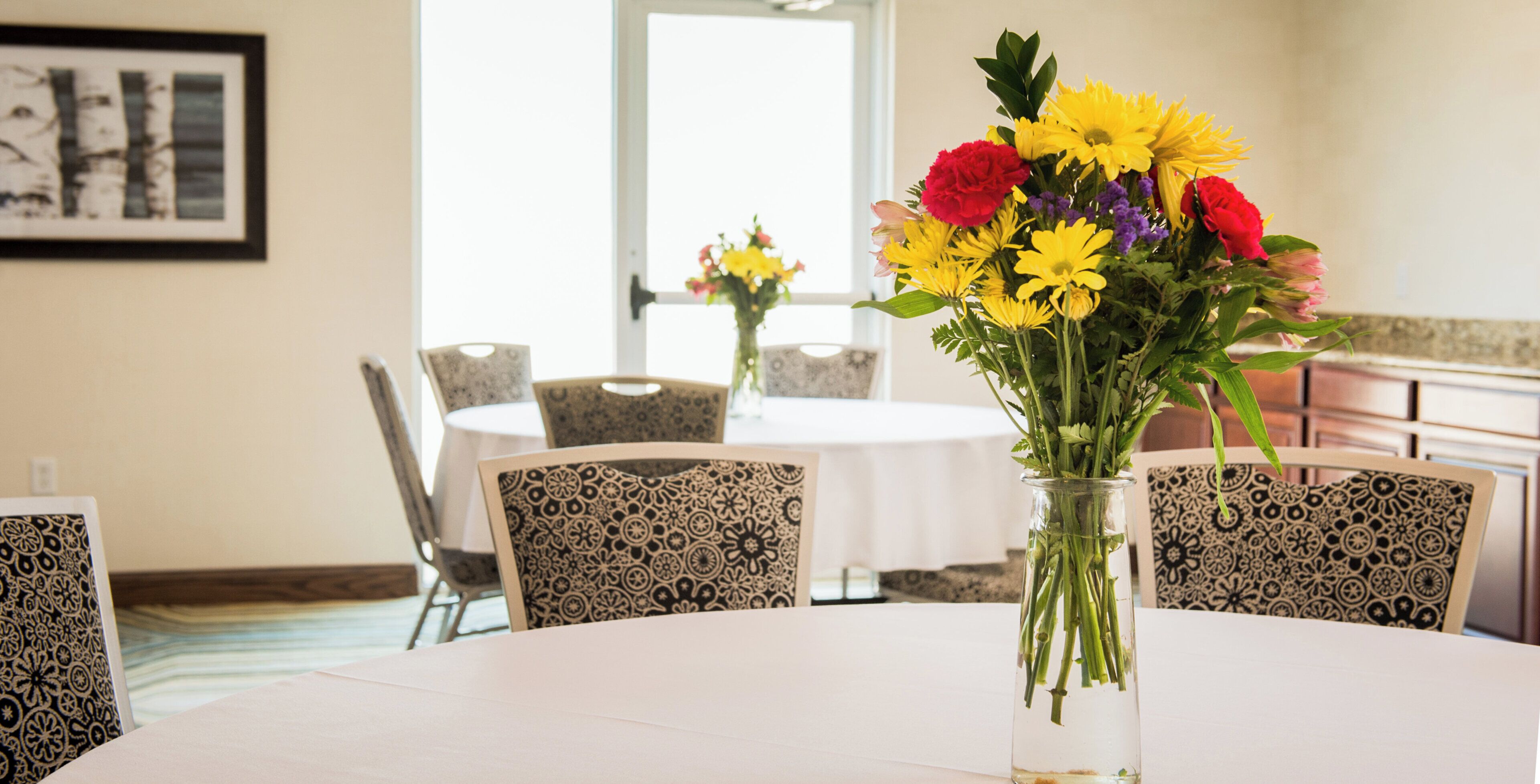 A dining area with a round table, chairs, and a vase of flowers.