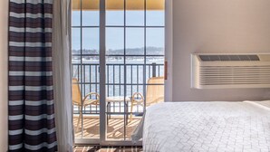 A hotel room with a bed, a window with a view of a snowy landscape, a balcony with chairs, and a wall-mounted air conditioner. - Holiday Inn Express Le Claire Riverfront-Davenport by IHG (Le Claire)