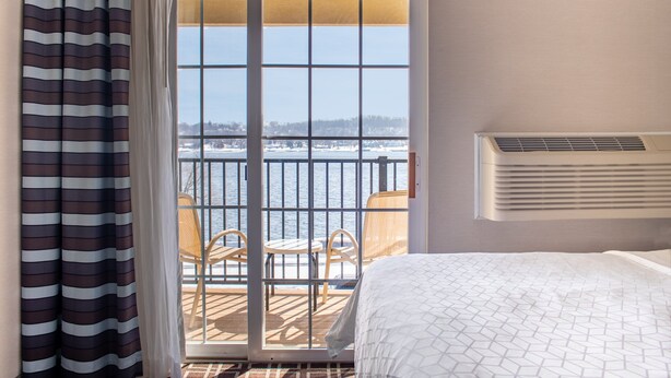 A hotel room with a bed, a window with a view of a snowy landscape, a balcony with chairs, and a wall-mounted air conditioner. - Holiday Inn Express Le Claire Riverfront-Davenport by IHG (Le Claire)