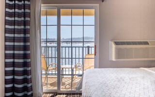 Una habitación de hotel con cama, ventana con vistas a un paisaje nevado, balcón con sillas y aire acondicionado de pared.
