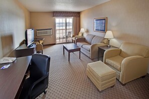 Habitación de hotel con escritorio, televisión, dos sillas, sofá, lámpara y ventana con vistas.