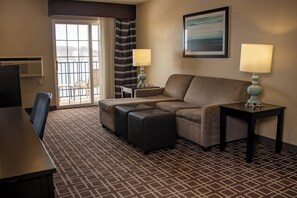 A hotel room with a sofa, ottoman, two lamps, a desk, and a chair.