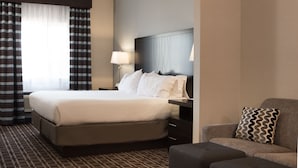 A hotel room with a large bed, a nightstand, a lamp, a sofa, and a patterned pillow. - Holiday Inn Express Le Claire Riverfront-Davenport by IHG (Le Claire)