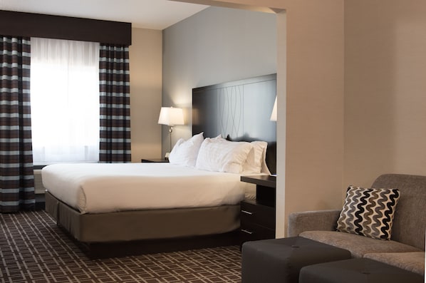 Una habitación de hotel con una cama grande, una mesita de noche, una lámpara, un sofá y un cojín estampado.