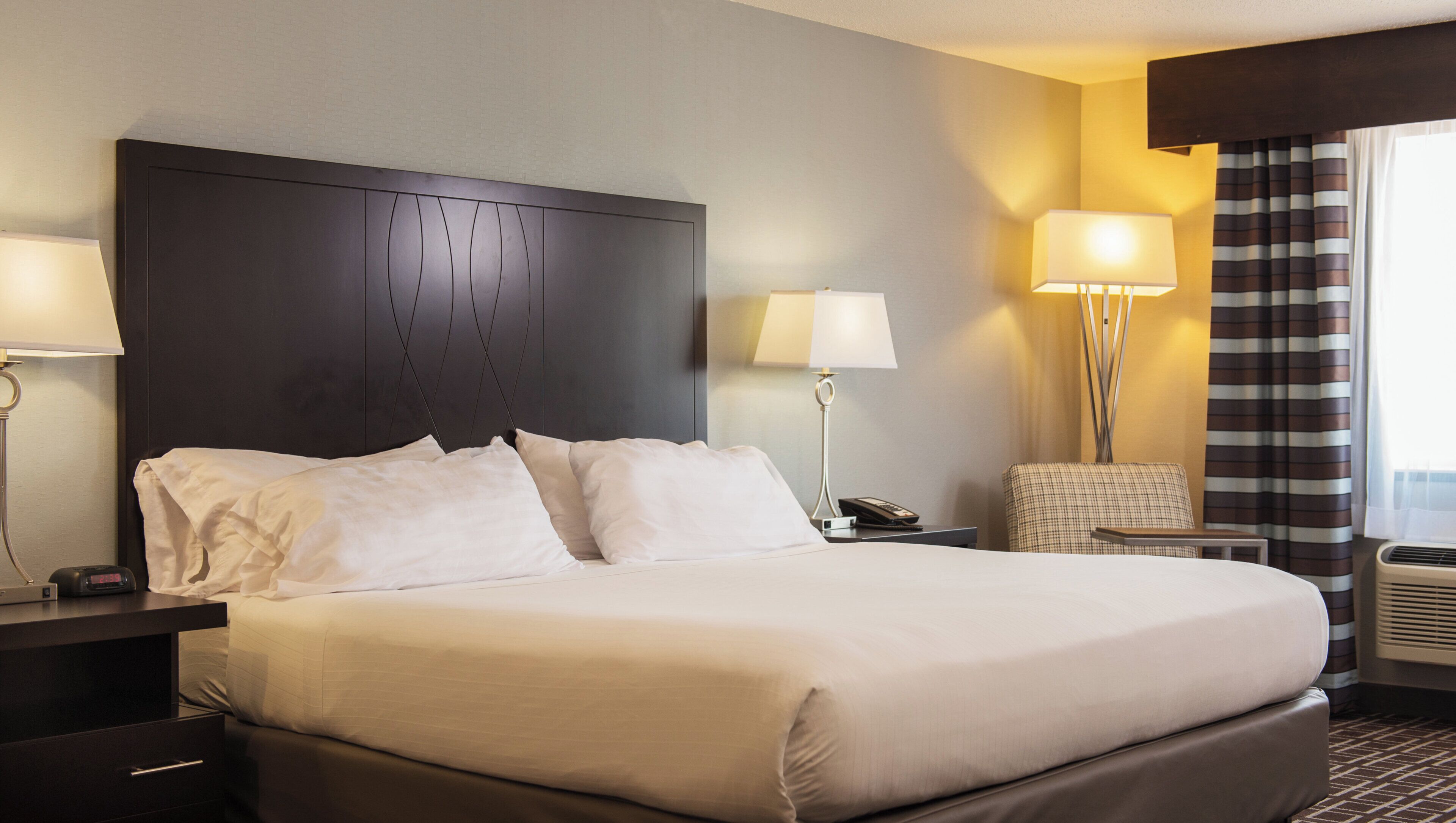Una habitación de hotel con una cama grande, una mesita de noche, una lámpara y una silla.