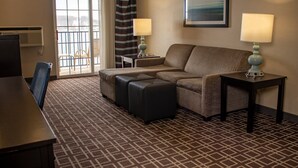 A hotel room with a sofa, ottoman, two side tables with lamps, a chair, a desk, and a large window with a view. - Holiday Inn Express Le Claire Riverfront-Davenport by IHG (Le Claire)