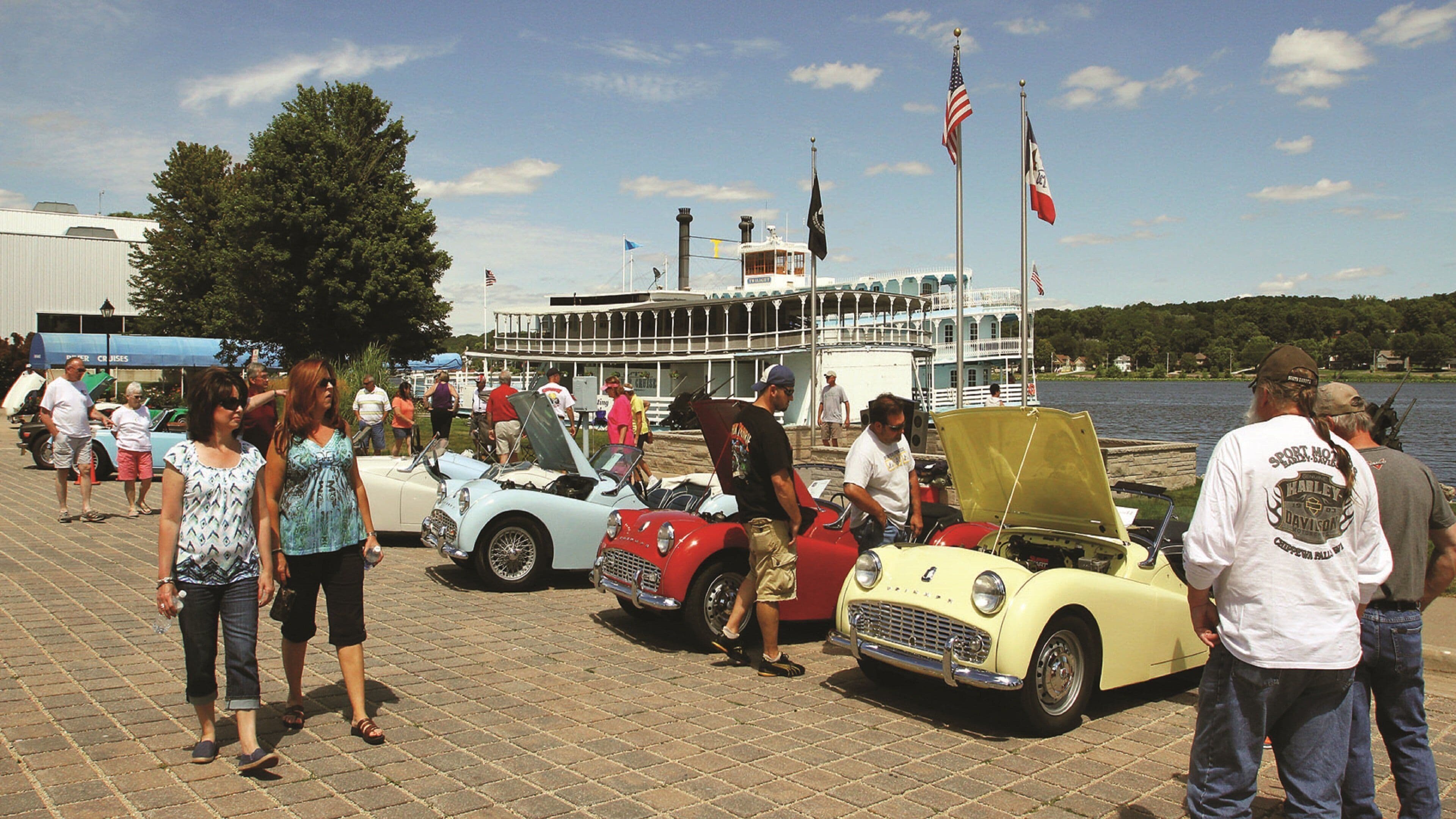 A waterfront event with vintage cars and a large boat in the background.