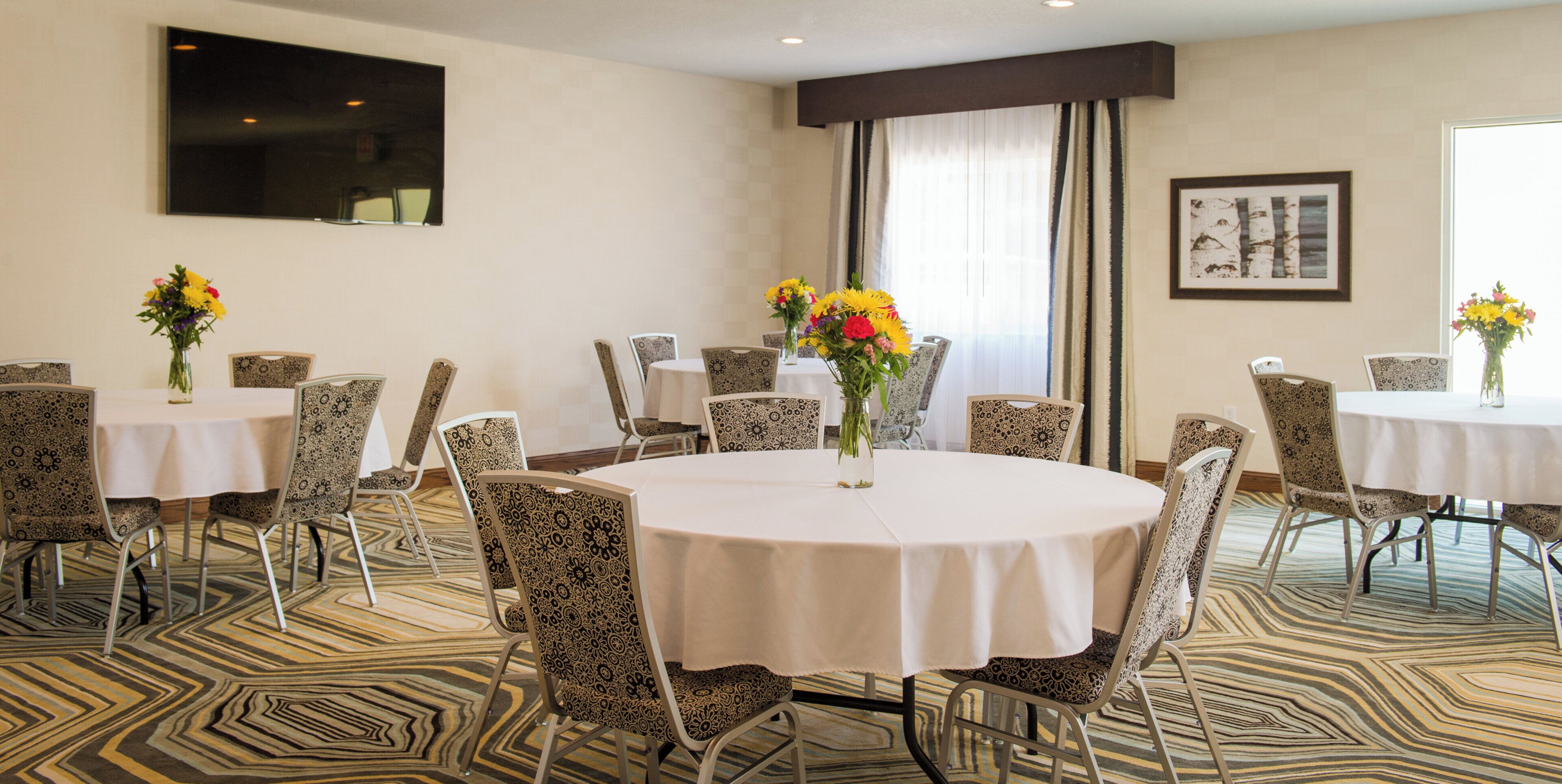 A conference room with round tables, patterned chairs, and floral centerpieces.
