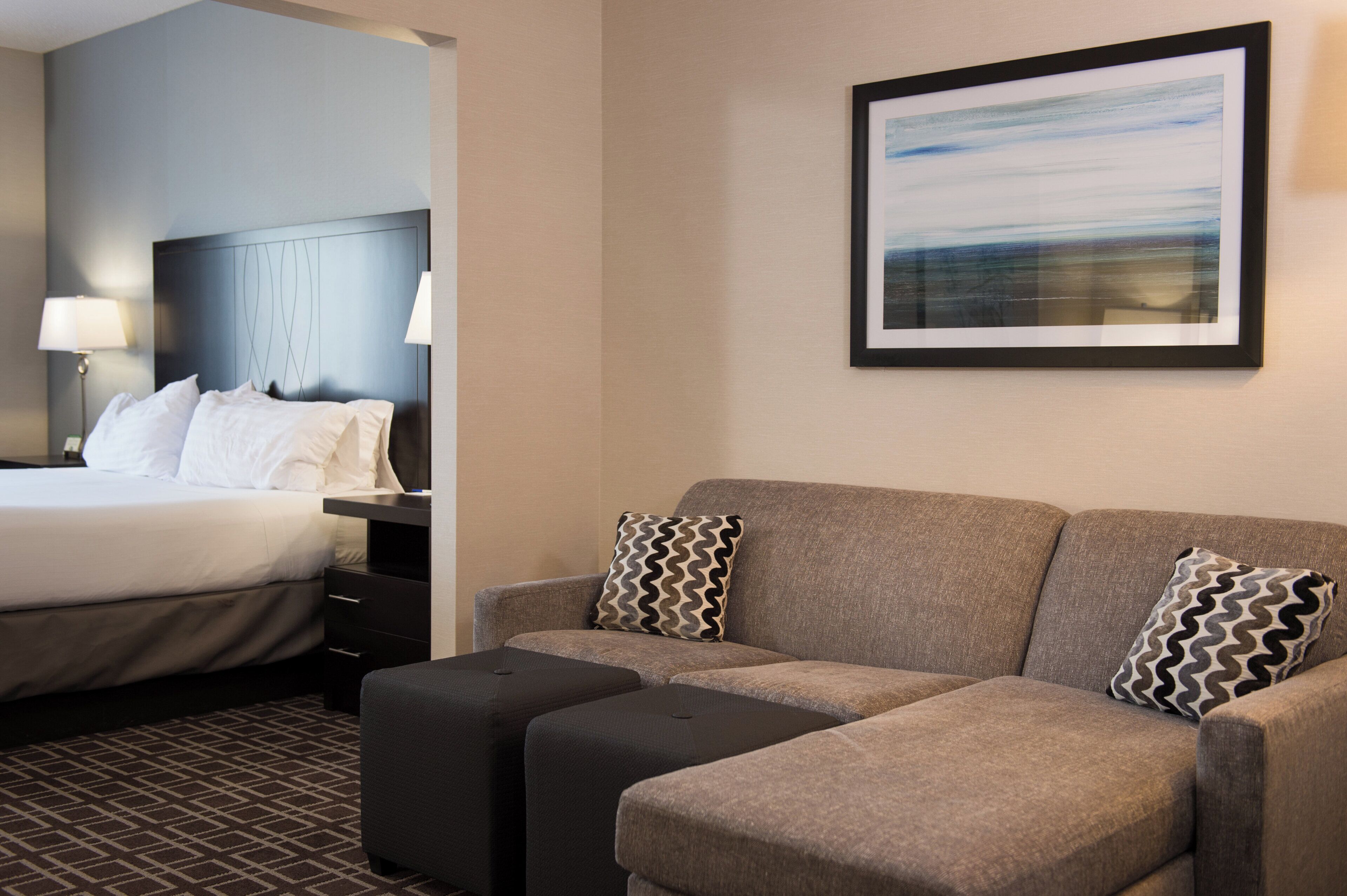 Quarto de hotel com cama, sofá, mesa de cabeceira, abajur e quadro na parede.