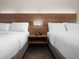 Habitación de hotel con dos camas, cabecera de madera, mesita de noche con teléfono y lámpara fijada a la pared.