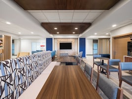 A conference room with a long wooden table, blue and grey chairs, and a large screen.