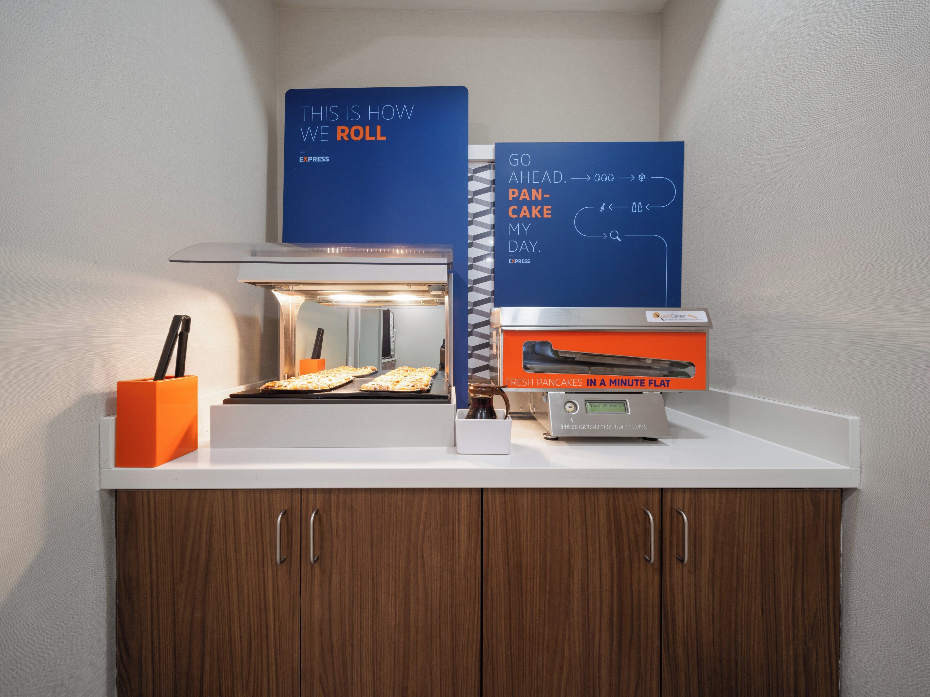A breakfast station with a flat-top griddle, a sign indicating how to order pancakes, and a digital display for the griddle's temperature.
