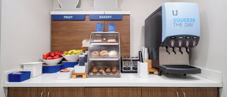 Un buffet pour le petit-déjeuner proposant des fruits, des viennoiseries, une machine à café et un saladier de produits frais.
