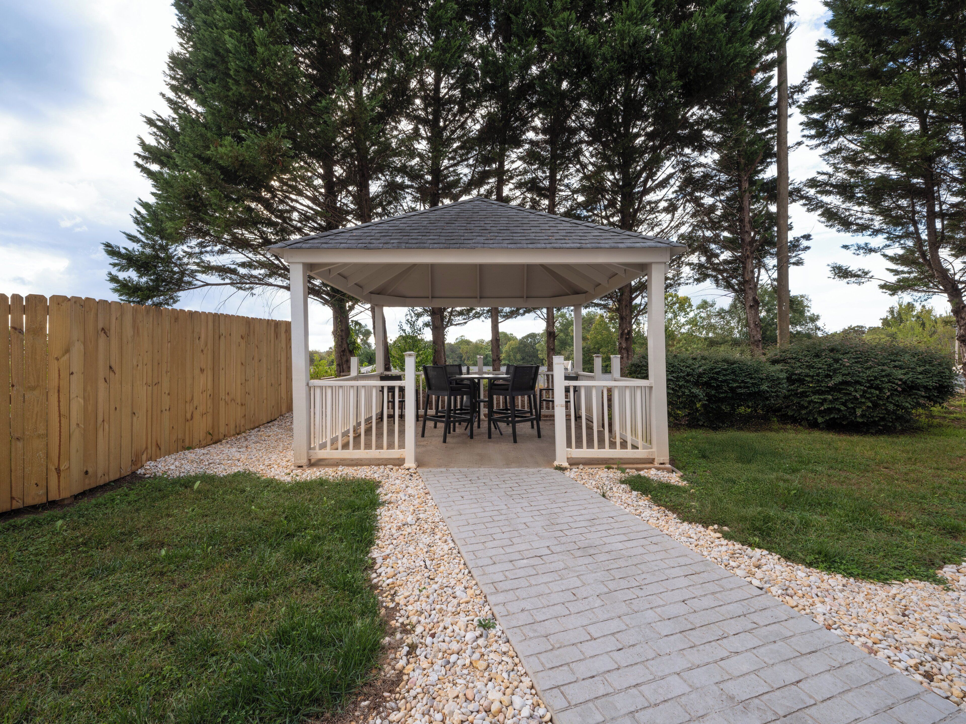 A covered patio with a table and chairs, surrounded by a wooden fence and trees.