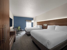 A hotel room with two beds, a desk, a chair, and a TV.