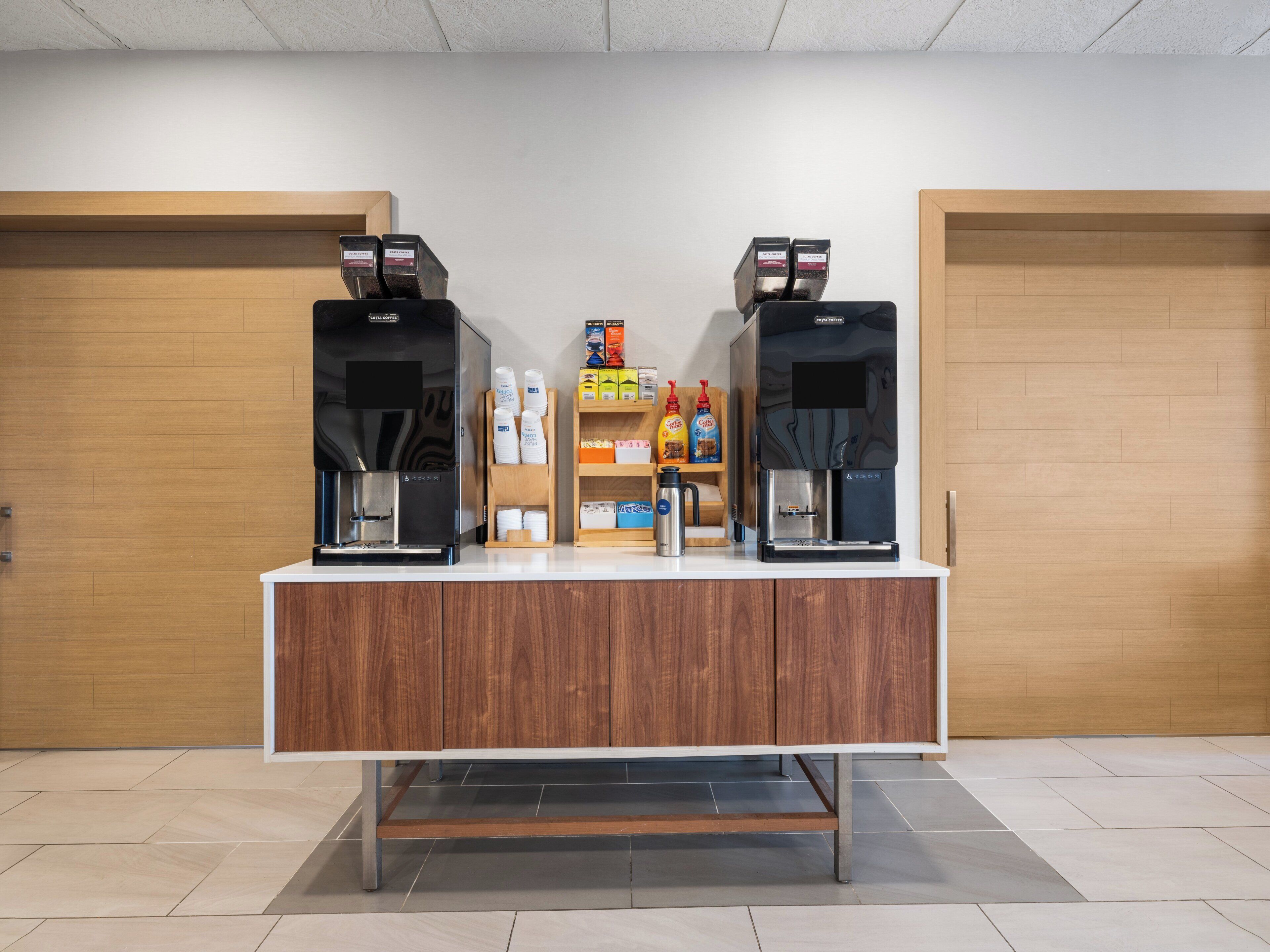 A coffee station with two espresso machines, a coffee dispenser, and various coffee products on a counter.