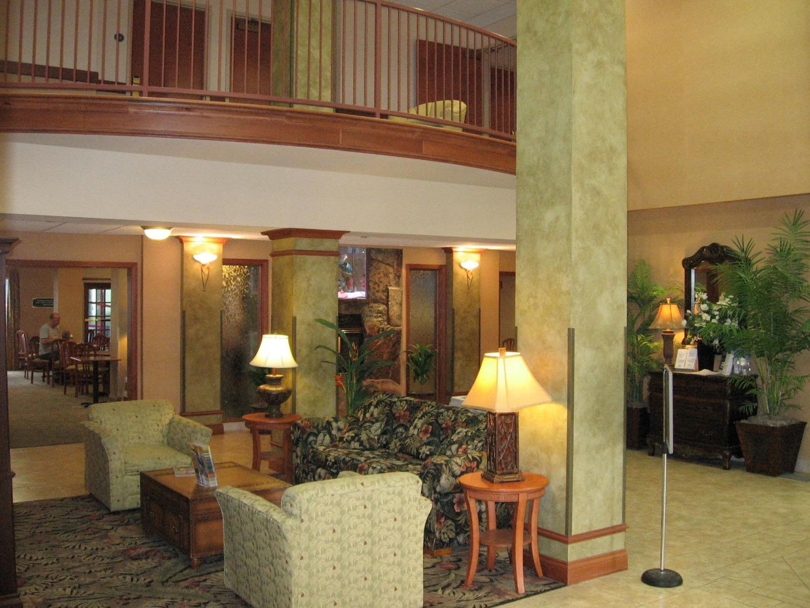 A lobby with a high ceiling, a balcony, and a seating area with chairs and a sofa.