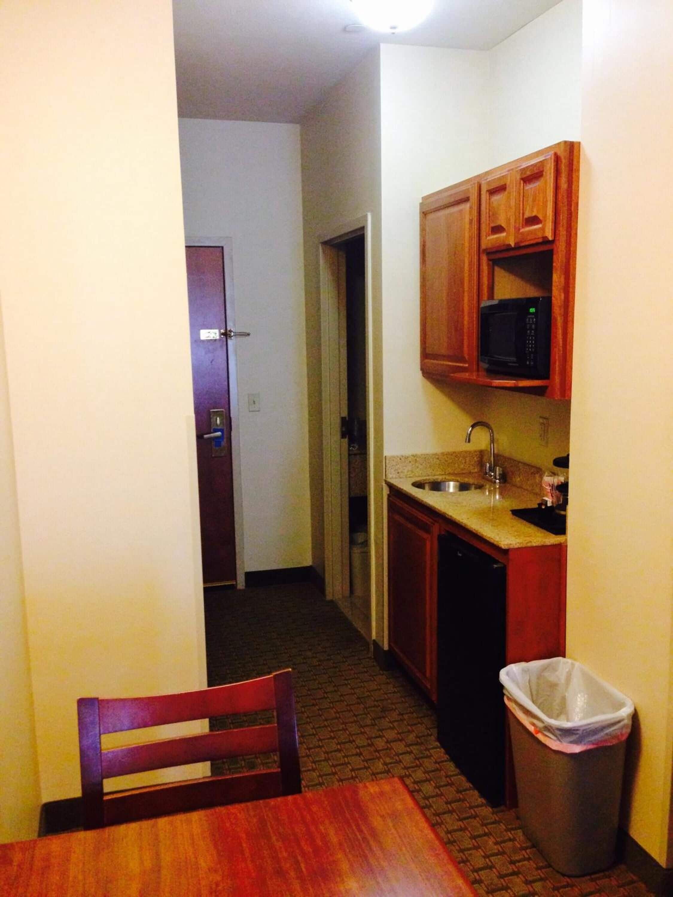 A compact kitchen with wooden cabinets, a microwave, a sink, and a trash can.