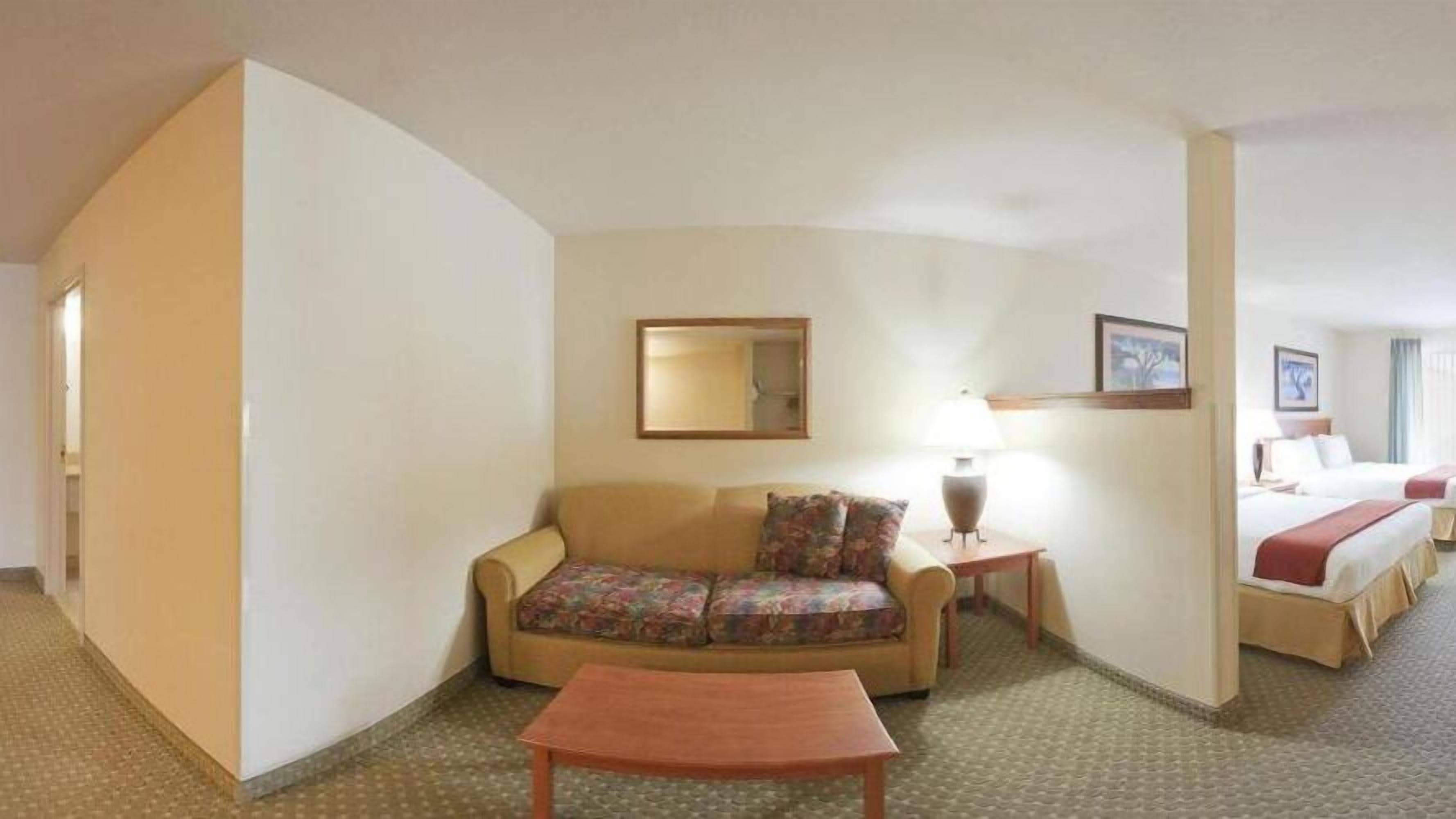 Une chambre d’hôtel avec un canapé, une petite table, une lampe, un lit et un tableau encadré au mur.