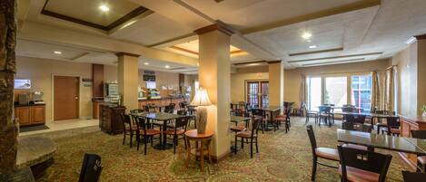 A spacious hotel lobby with multiple dining areas, a reception desk, and a buffet.