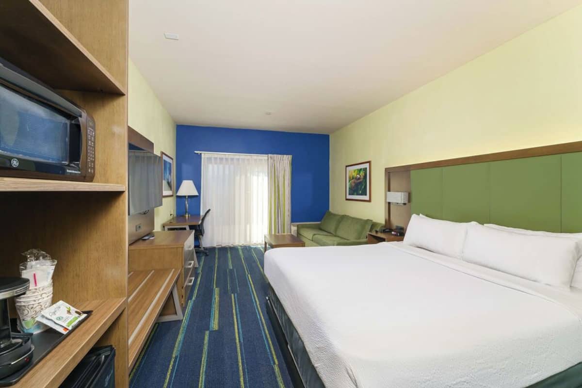 A hotel room with a bed, a desk with a computer, a microwave, and a television.
