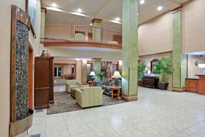 A spacious lobby with a high ceiling, a central seating area with sofas and a coffee table, a reception desk, and a staircase leading to an upper level. - Triple Play Resort Hotel & Suites (Hayden)