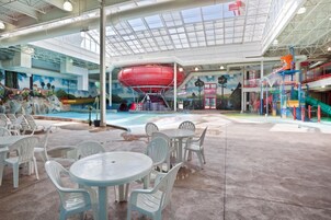 Parque acuático interior con un tobogán de agua grande, zonas de estar y un mural que representa un paisaje tropical.