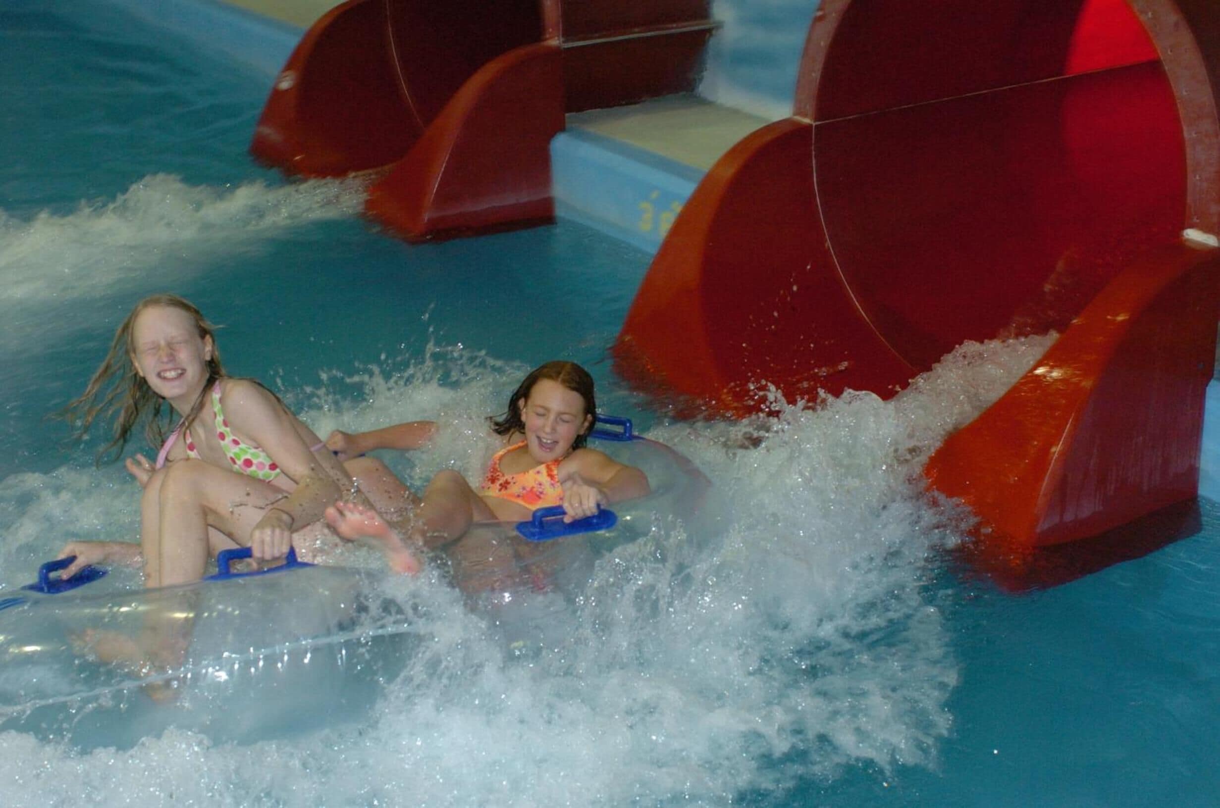 Two people in an indoor water slide with clear water and red slides.