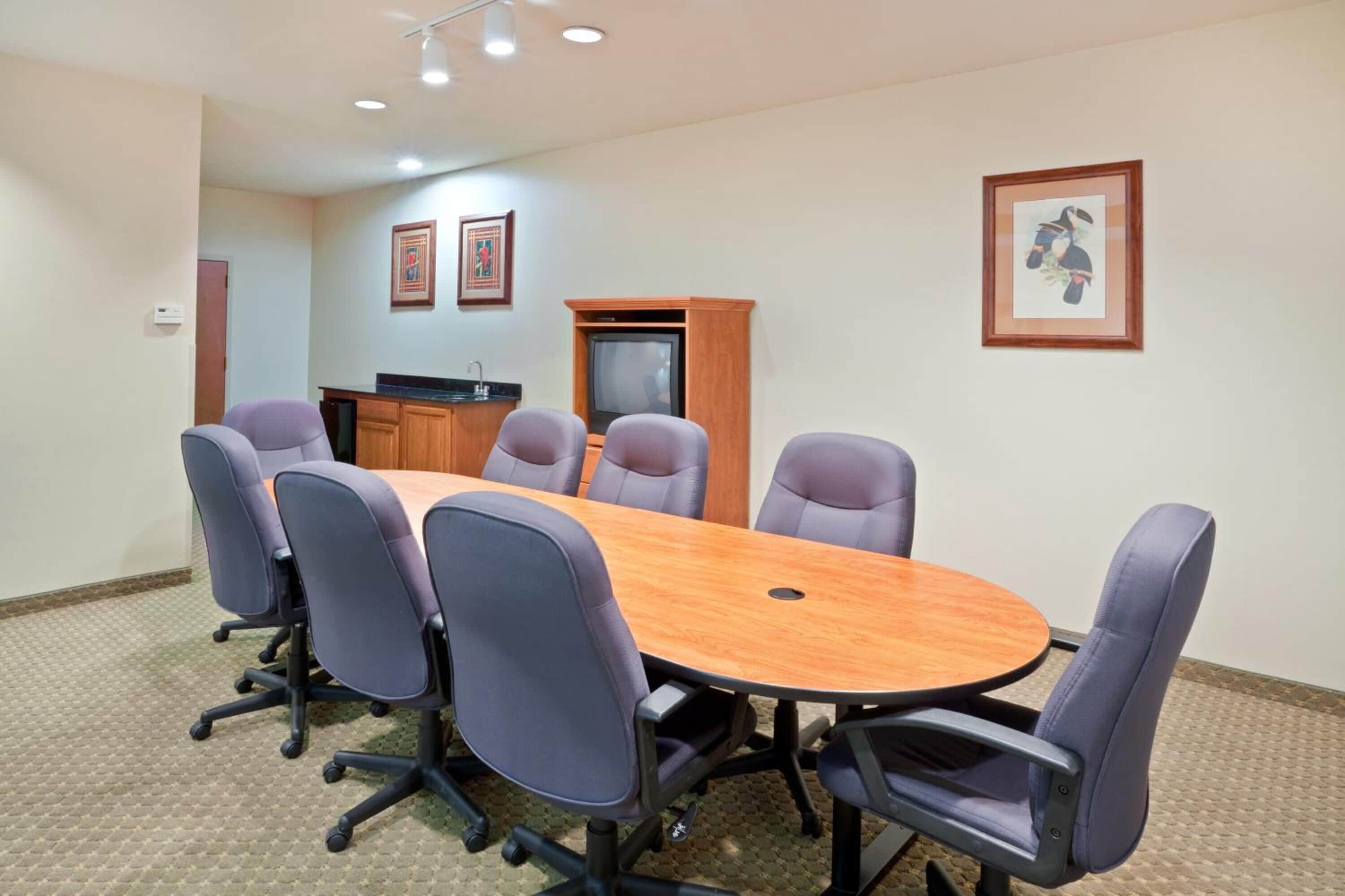 Une salle de conférence avec une table en bois, six chaises, un téléviseur et des tableaux encadrés aux murs.