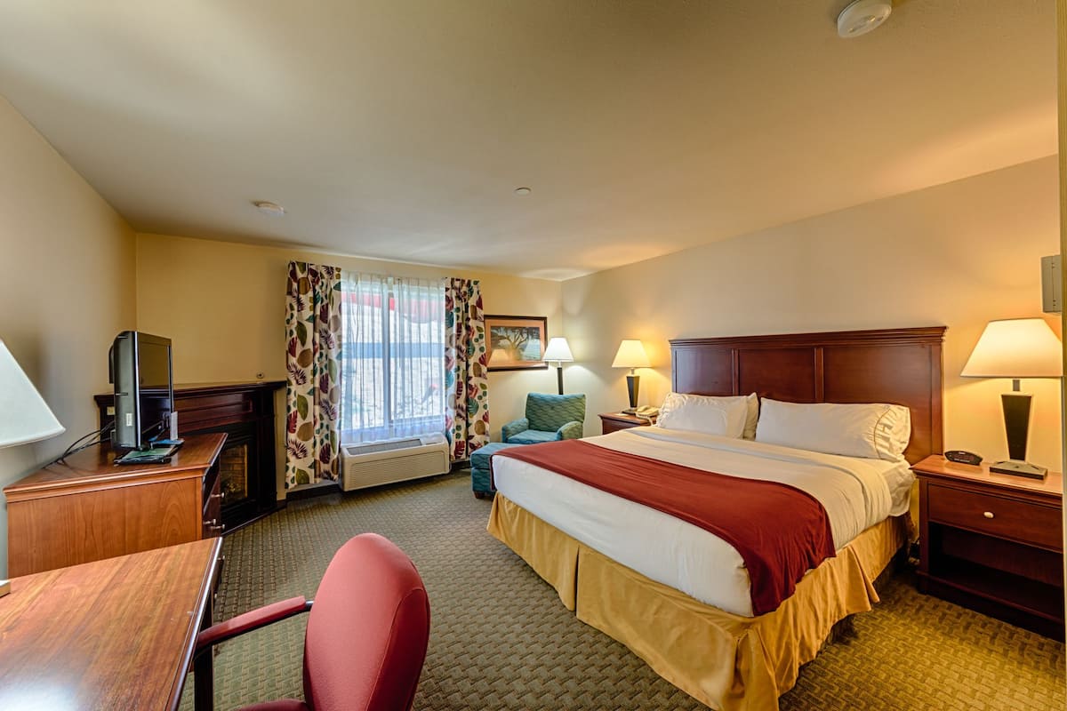 A hotel room with a bed, desk, chair, and a window with curtains.