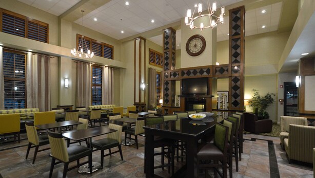 A spacious dining area with multiple tables and chairs, a large chandelier, and a clock on the wall. - Hampton Inn & Suites Carson City (Carson City)