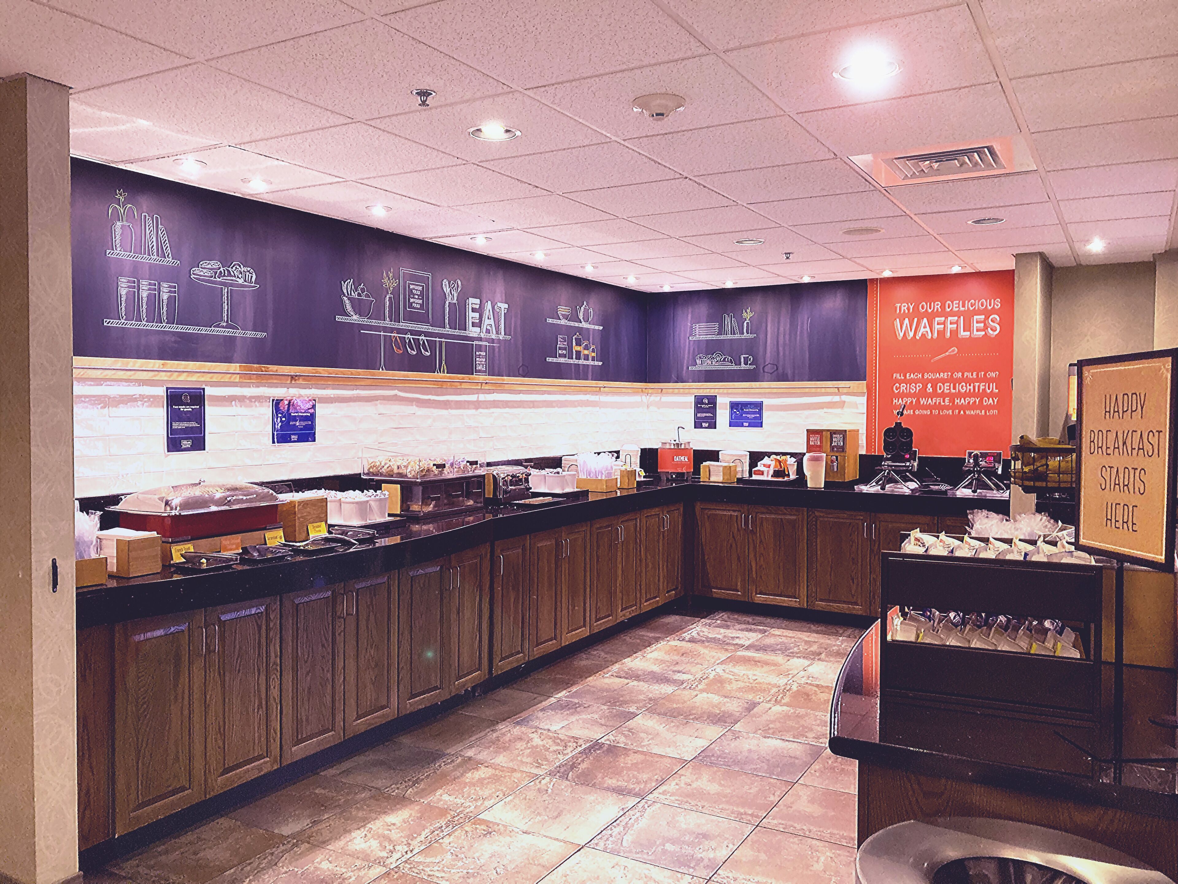 A breakfast buffet area with a variety of food items and a sign advertising waffles.