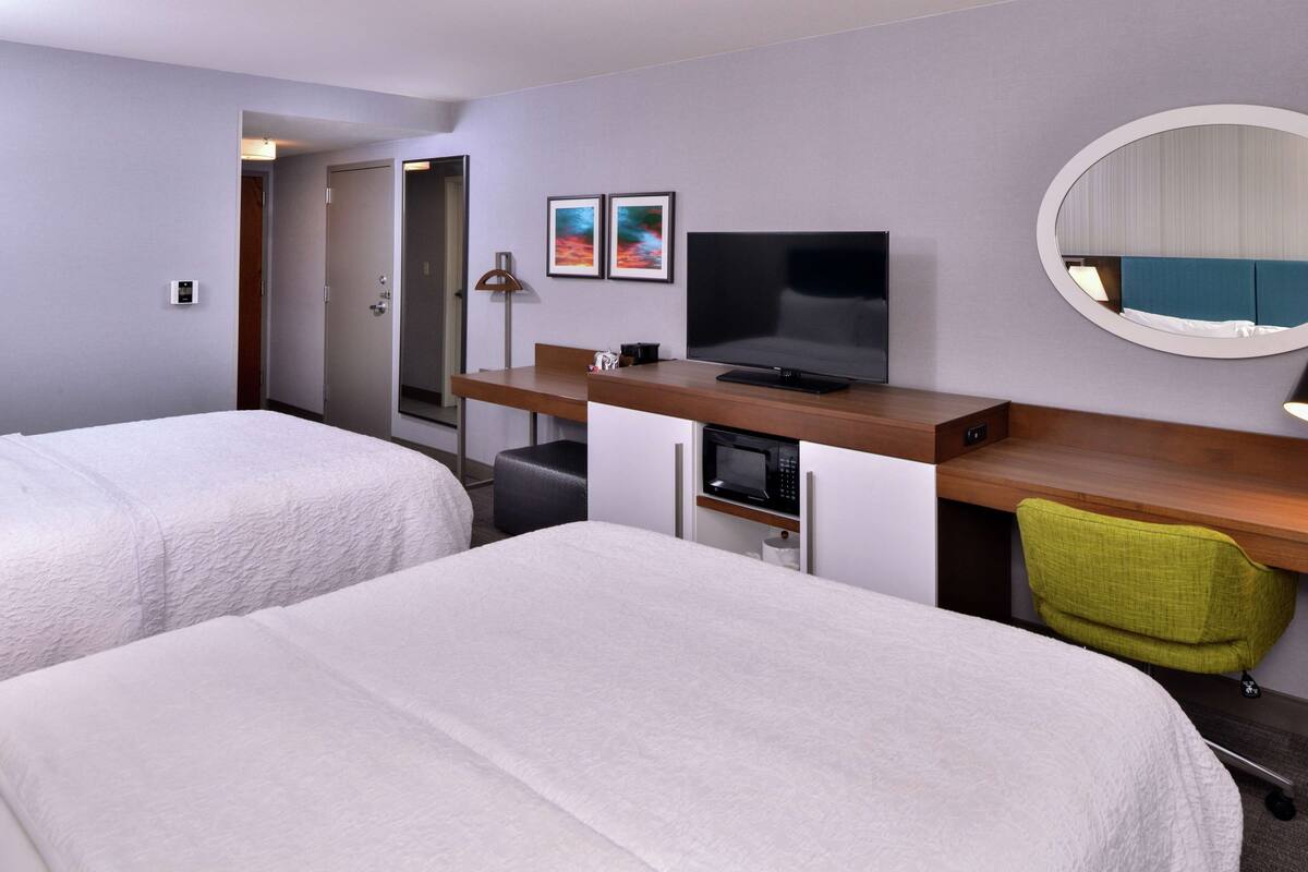 A hotel room with two beds, a desk with a TV, a microwave, and a mirror.