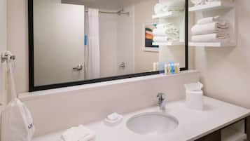 Une salle de bain avec un grand miroir, un lavabo, un porte-serviettes et une étagère où sont pliés les serviettes.