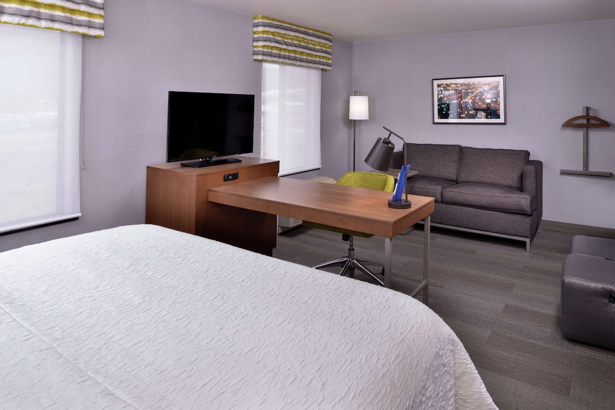 A hotel room with a bed, a desk with a TV, a sofa, and a cityscape picture on the wall.