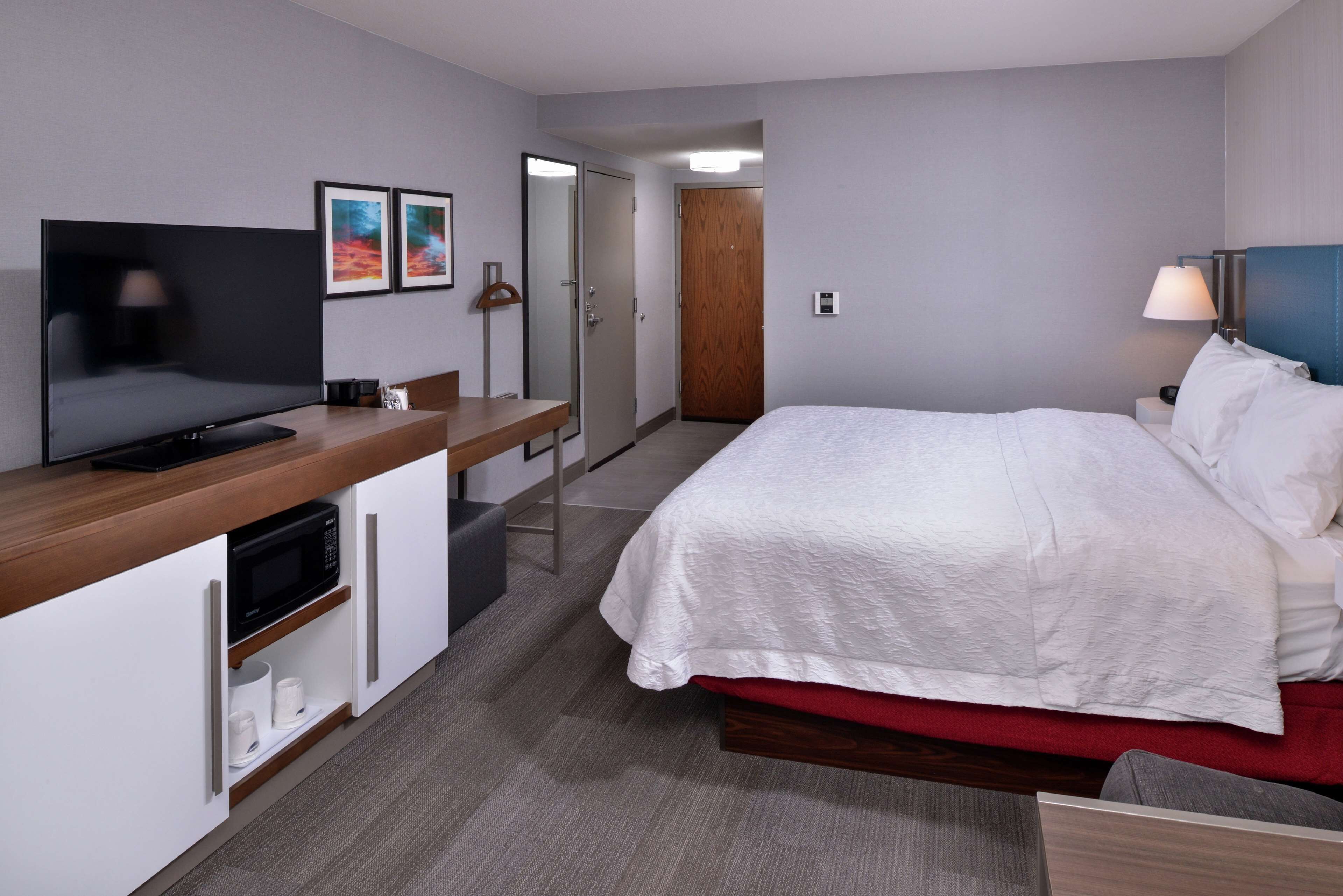 A hotel room with a bed, a TV, a microwave, a desk, and a door leading to another room.