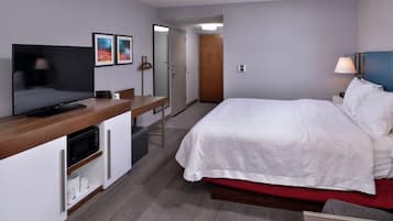 A hotel room with a bed, a TV, a microwave, a desk, and a door leading to another room.