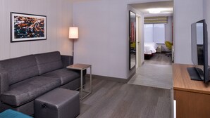 A modern hotel room with a grey sofa, a small table, a TV, and a bed with a yellow chair. - Hampton Inn & Suites Carson City (Carson City)