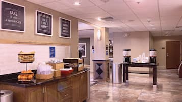 Um saguão de hotel com balcão de recepção, placas na parede e um espaço para café.