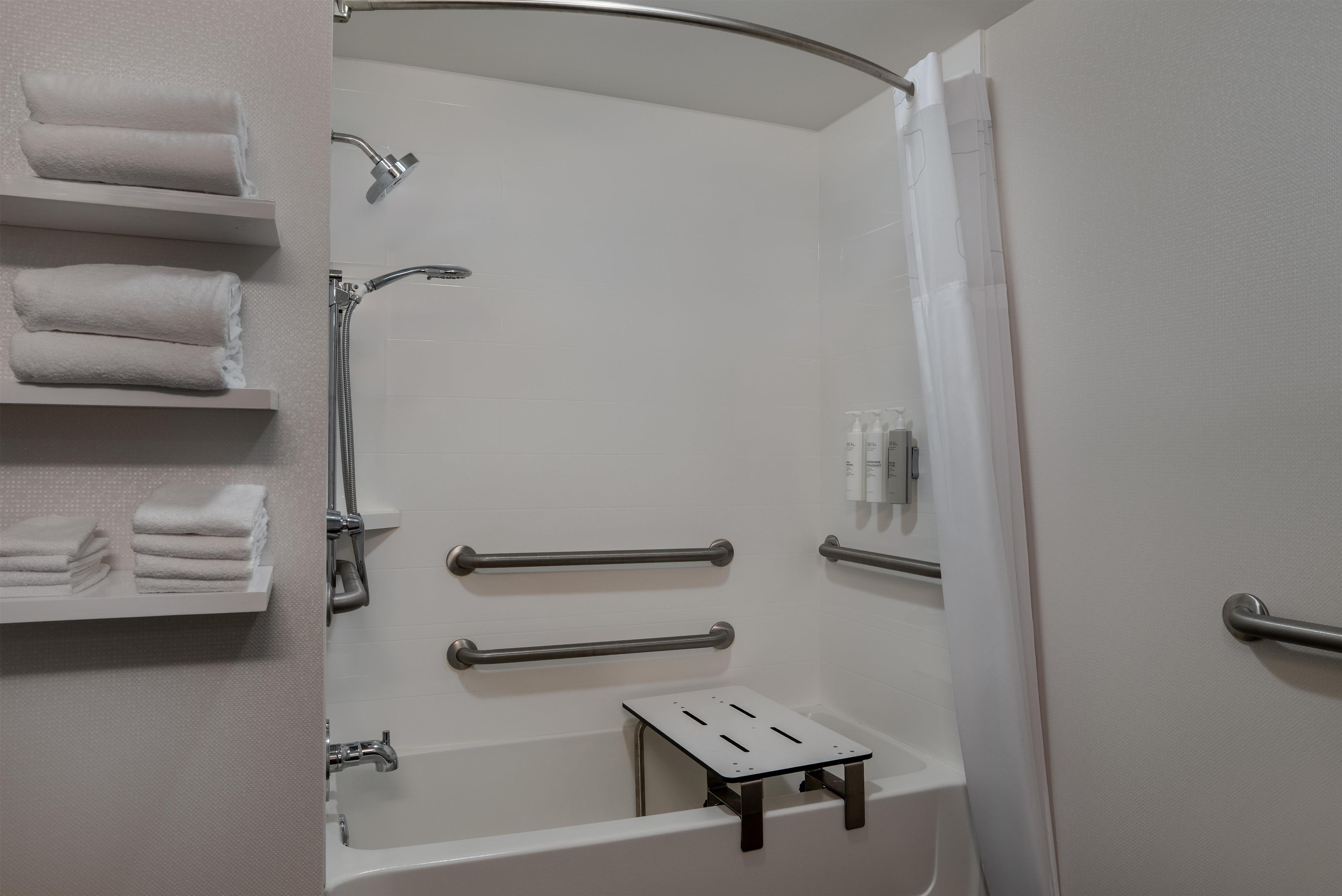 A modern bathroom with a shower, grab bars, a towel rack, and a small table.