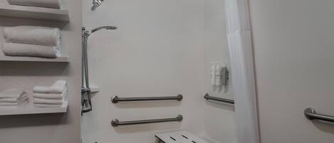 A modern bathroom with a shower, grab bars, a towel rack, and a small table.