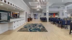 A hotel lobby with a reception desk, seating area, and a view of the kitchen in the background.