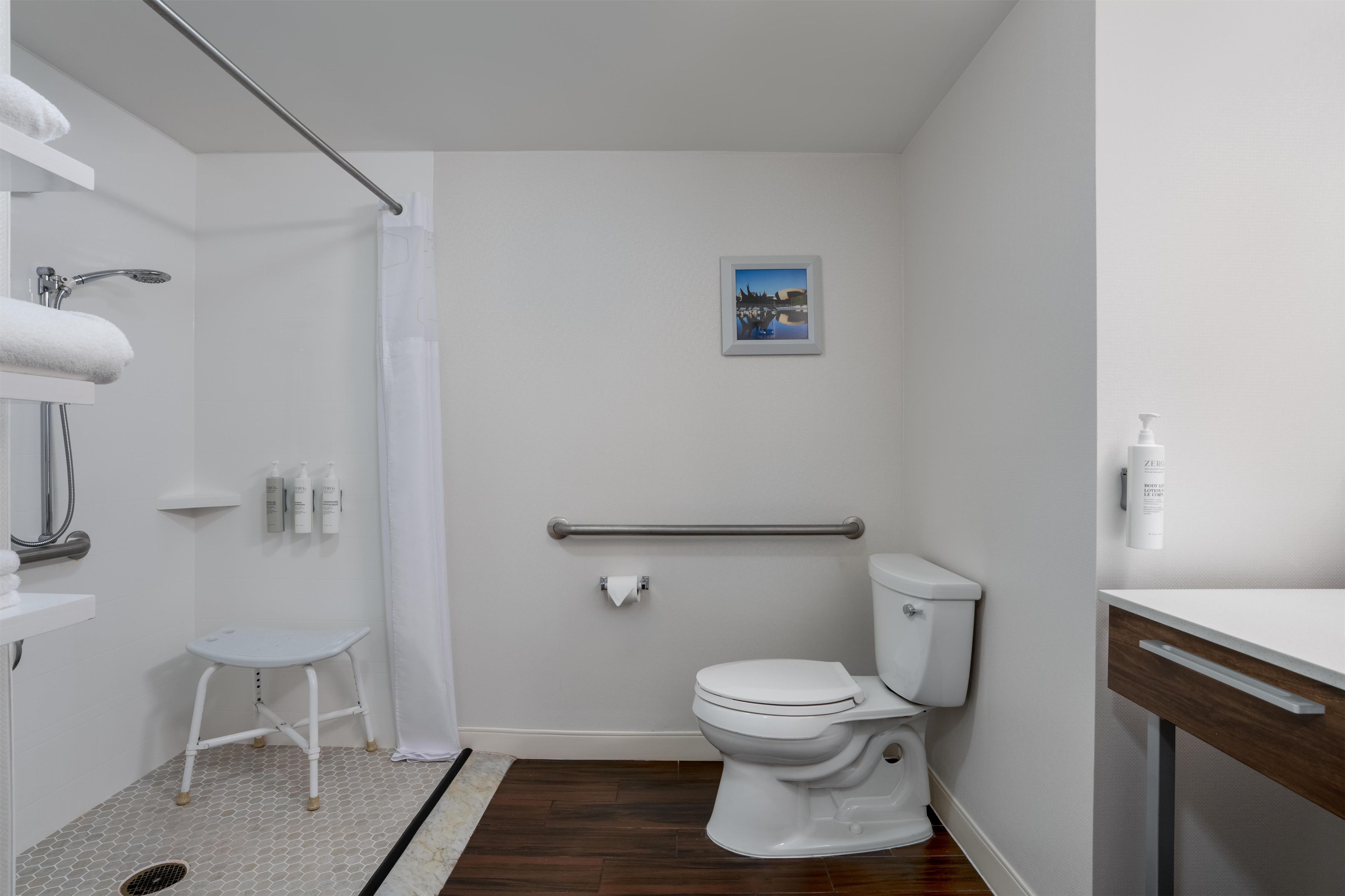 A modern bathroom with a shower, toilet, and a small stool.