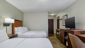 Habitación de hotel con dos camas, un escritorio, televisión, lámpara y una puerta que da a otra habitación.